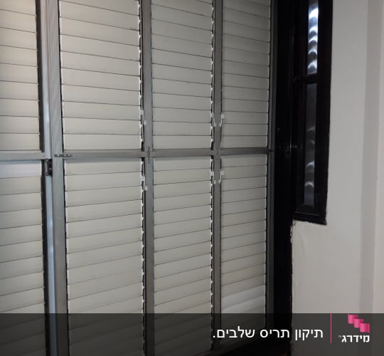 תריסים לבנים עם מסגרת מתכת בחלון פנימי